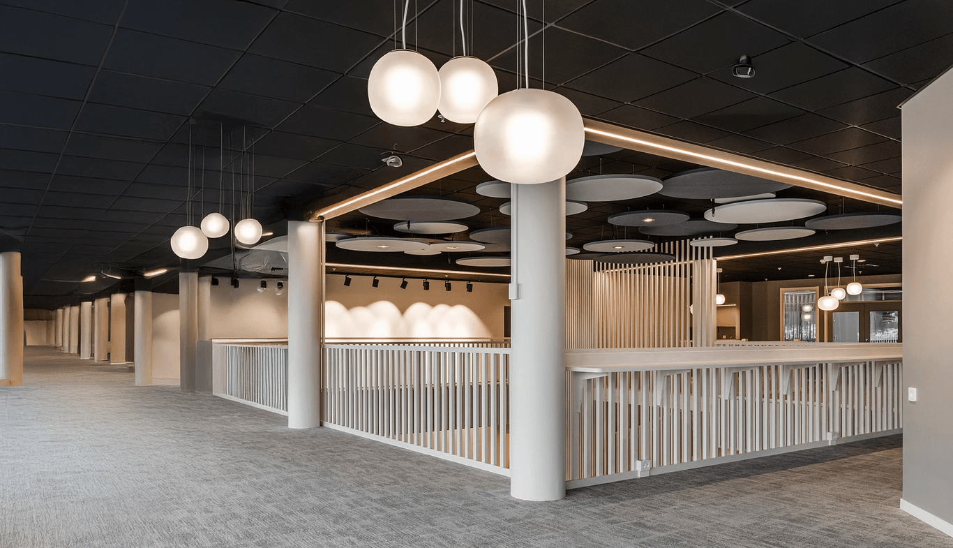 Modern kontorsinredning med runda taklampor, vita räcken och grå heltäckningsmattor.